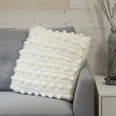 a white crocheted pillow sitting on top of a gray couch