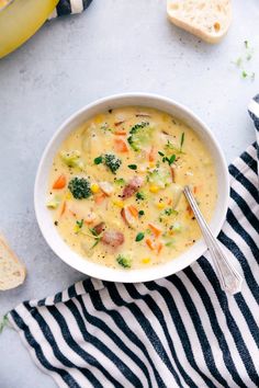 a bowl of soup with broccoli, carrots and bread on the side