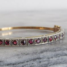 This lovely vintage bangle was crafted around 1940 of 18k gold, silver, and fifteen red spinels. Red spinel was historically mistaken for either ruby or garnet, and has a rich history dating back centuries. In fact, it is a large red cabochon spinel, mistaken for ruby, which constitutes the "Black Prince's Ruby" in the British Crown. Its true identity as a separate gemstone didn't emerge until in the 19th century.  The red spinels in this lovely bangle are of mixed cuts and colors, some a deeper Antique 14k Stamped Bangle As Gift, Vintage Hand Set Yellow Gold Jewelry, Antique 17 Jewels Bracelet For Anniversary, Vintage Hand Set Bracelets For Formal Occasions, Art Deco Yellow Gold Bracelets For Formal Occasions, Vintage 14k Gold Bracelet For Anniversary, Vintage Formal Bracelets, Heirloom 14k Gold Bangle With 17 Jewels, Classic Formal Bangle With Gemstone