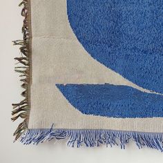 a blue and white area rug with fringes on the bottom, in front of a white wall