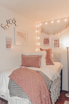 a white bed topped with pillows and blankets next to a wall covered in string lights