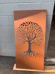 an orange metal sign with a tree cut out on it's side next to a brick wall