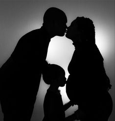 a man and woman kissing in front of the sun with their shadow on the wall