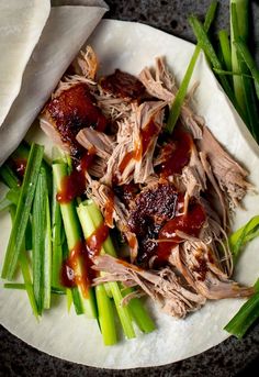 a white plate topped with meat and veggies covered in bbq sauce next to green beans