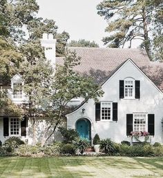 a large white house with black shutters and green front door is surrounded by trees