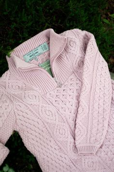 a pink sweater laying on the ground in front of some green grass and bushes with a tag attached to it