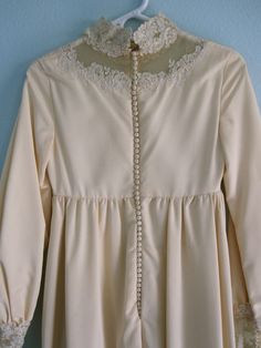 "Lovely 60s wedding dress in a classic empire waist style - I think the high neck, empire waist, and long sleeves give it a dramatic, medieval look. It's made of ivory silk faille and trimmed with lace and mesh at the neckline and wrists. The back of the gown has a whopping 53 silk covered buttons and each wrist has 14 buttons, for a total of 81 buttons (it took me several minutes to button it all up, and any wearer will need an assistant to get into this one). The gown is lined with muslin, exc Classic A-line Vintage Wedding Dress, Vintage Empire Waist Dress For Wedding, Vintage A-line Wedding Dress With Fitted Bodice, Elegant Vintage Dress With Lace Bodice For Wedding, Retro Vintage Wedding Dress With Lace Trim, Elegant Vintage Wedding Dress With Lace Bodice, Fitted Vintage Dress With Lace Bodice For Wedding, Cream Vintage Dress With Fitted Bodice For Weddings, Fitted Vintage Dress For Wedding