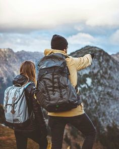 two people with backpacks looking at the mountains