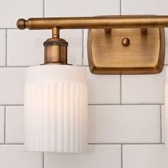 two light fixtures mounted on a white tile wall in a bathroom with gold fittings