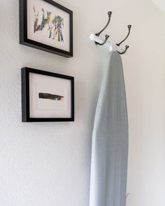 two framed pictures hang on the wall next to an ironing board and towel rack