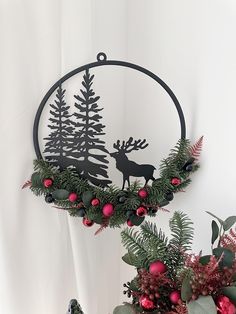 a metal deer and pine tree decoration hanging on a wall next to christmas greenery