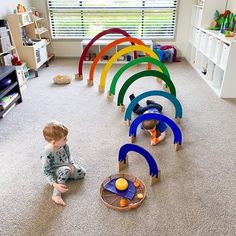 a toddler playing with toys in a playroom on the floor next to a window