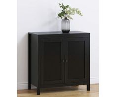 a black cabinet with two doors and a vase on it's top, in front of a white wall