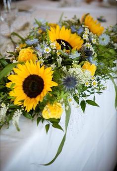 a bouquet of sunflowers and other flowers are on a table with white linen