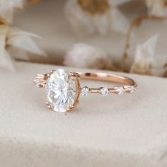 a close up of a diamond ring on a white surface with flowers in the background