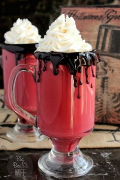 two red mugs with whipped cream and chocolate drizzled on the top