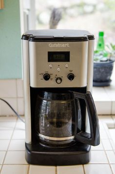 a coffee maker sitting on top of a white tile floor next to a potted plant