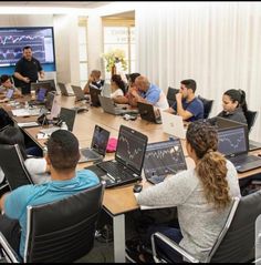 a group of people sitting around a conference table with laptops and monitors on it