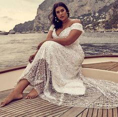 a woman sitting on the back of a boat in a white dress with sequins