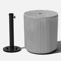 a white trash can sitting next to a black metal pole on a white surface with a shadow from the floor