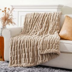 a white couch with a blanket on top of it next to a brown pillow and vase