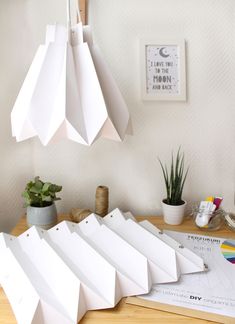 several white paper pieces on a table with plants and other items in the room behind them