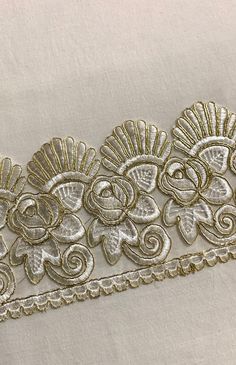 a white and gold lace trim with flowers on the side is laying on top of a piece of cloth