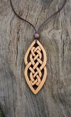 a wooden pendant with an intricate design on a leather cord hanging from a piece of wood