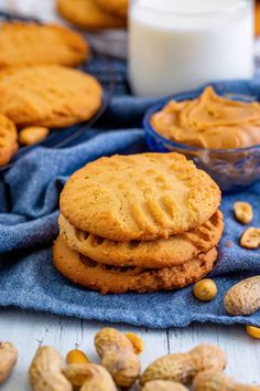 peanut butter cookies stacked on top of each other next to some peanuts and a glass of milk