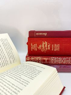 three red books sitting next to each other on top of a white table with an open book in front of them