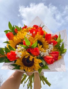 a bouquet of sunflowers and tulips is being held by someone's hand