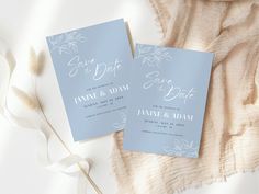 two blue wedding cards sitting on top of a white blanket