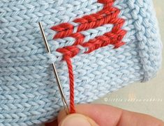 someone is stitching the stitches on a blue knitted hat with a red thread