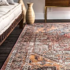 a large area rug with an orange and brown design on the center, in front of a bed