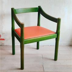 a green chair with an orange seat sits on a tile floor in front of a white wall