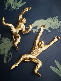 two gold monkey brooches laying on top of a blue background with green and white wallpaper