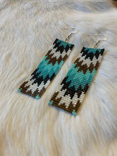 a pair of earrings on top of a white fur covered animal print rug with black and blue beads