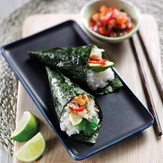 two sushi rolls on a black plate with chopsticks next to it and a bowl of salsa