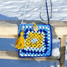 a crocheted purse hanging on a wooden bench in the snow with a tasseled handle