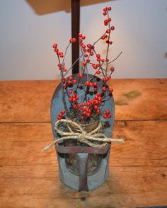 a vase filled with red berries sitting on top of a wooden table next to a lamp