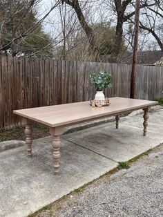 a wooden table sitting on top of a cement ground next to a fence and trees