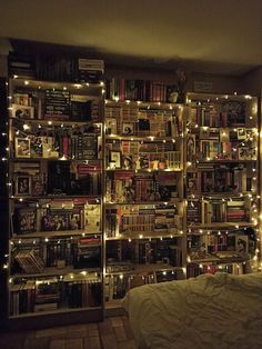 a book shelf filled with lots of books covered in fairy lights next to a bed