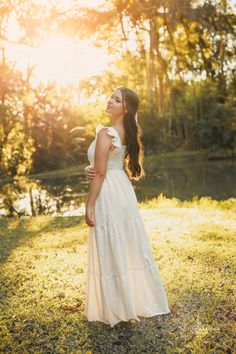 a woman in a white dress is standing on the grass near trees and looking up into the sky