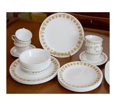 an assortment of white and gold dinnerware on a wooden table top with plates, cups, and saucers