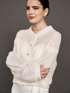 a woman with her arms crossed wearing a white sweater