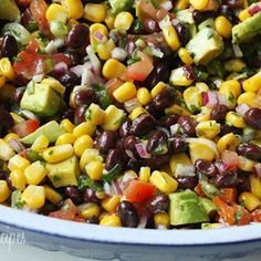 a bowl filled with black beans, corn and avocado salad on top of a white table