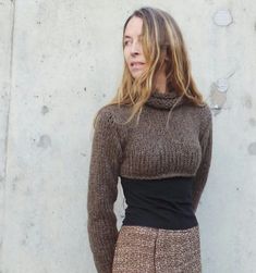 a woman standing in front of a concrete wall wearing a brown sweater and skirt with high waist