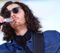 a man with long curly hair and sunglasses holding a cell phone to his ear while standing in front of a microphone