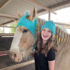 a girl standing next to a horse wearing knitted hats