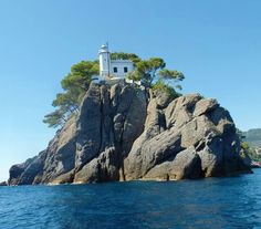 an island with a lighthouse on top of it in the middle of the ocean, surrounded by trees